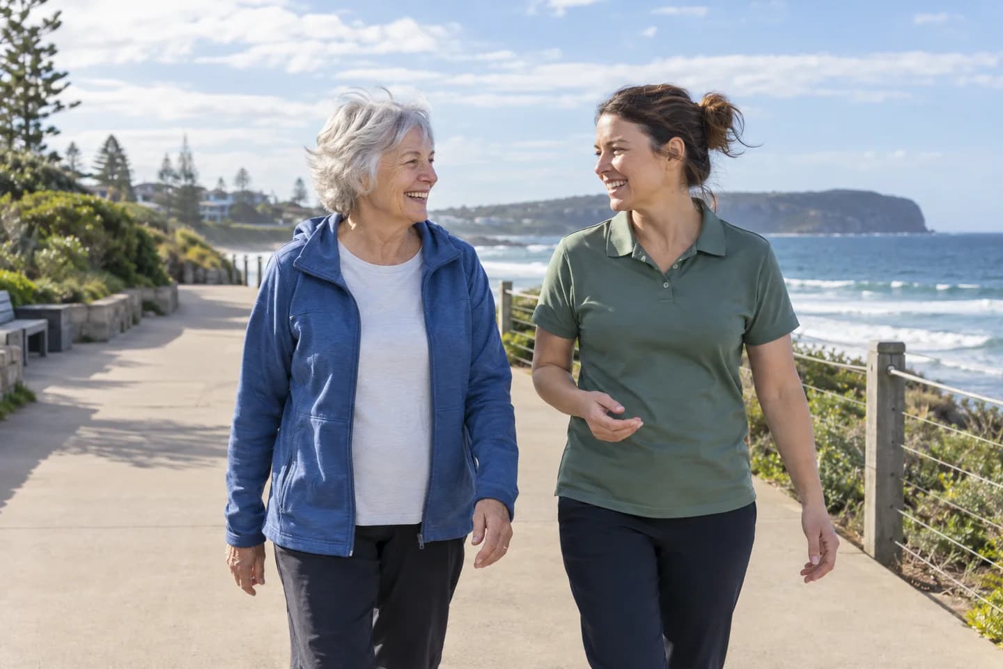 Support worker and older woman laughing together on a sunny coastal walk
