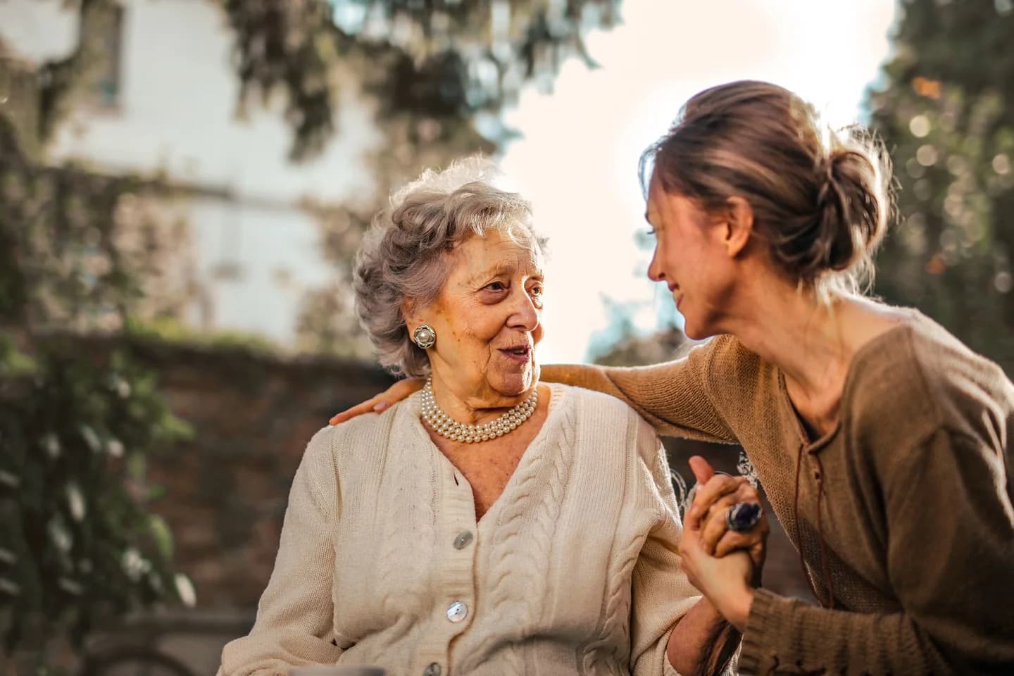 Older woman and adult daughter smiling and holding hands in a garden