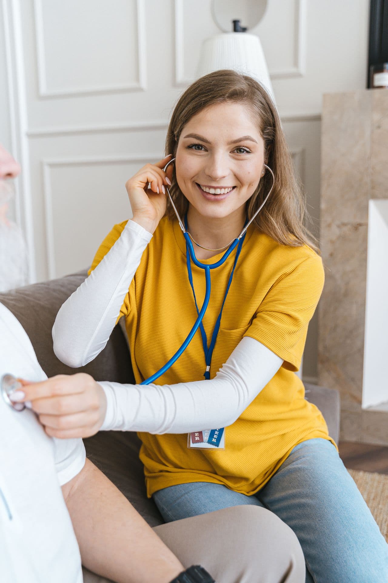Smiling nurse listening with a stethoscope during a home visit in a bright living room